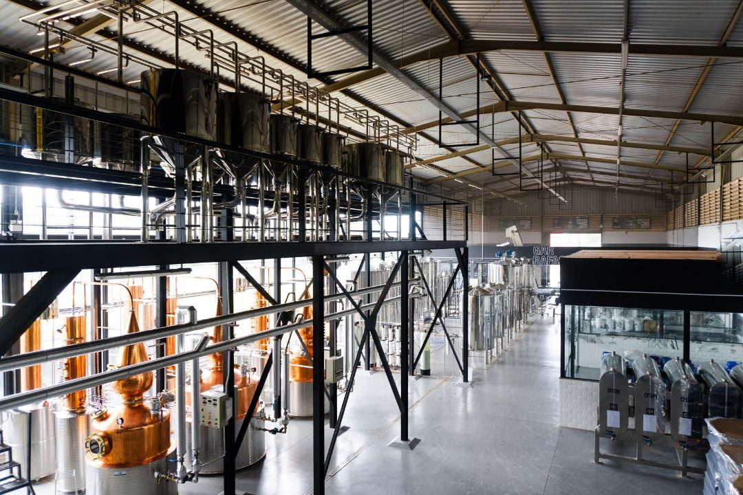 Interior industrial da destilaria: tanques inox e alambiques